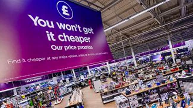 Inside of a Currys store, a giant banner with 'You won't get it cheaper' written on it hangs from the ceiling.