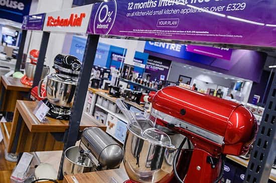A range of different, brightly coloured food mixers on display, inside a Currys store.
