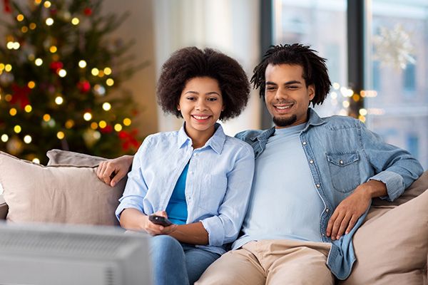 A couple watching TV with a Christmas tree behind them